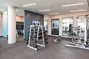 Ein modernes Fitnessstudio mit Krafttrainingsgeräten, Cardiogeräten und einem Fernsehbildschirm.