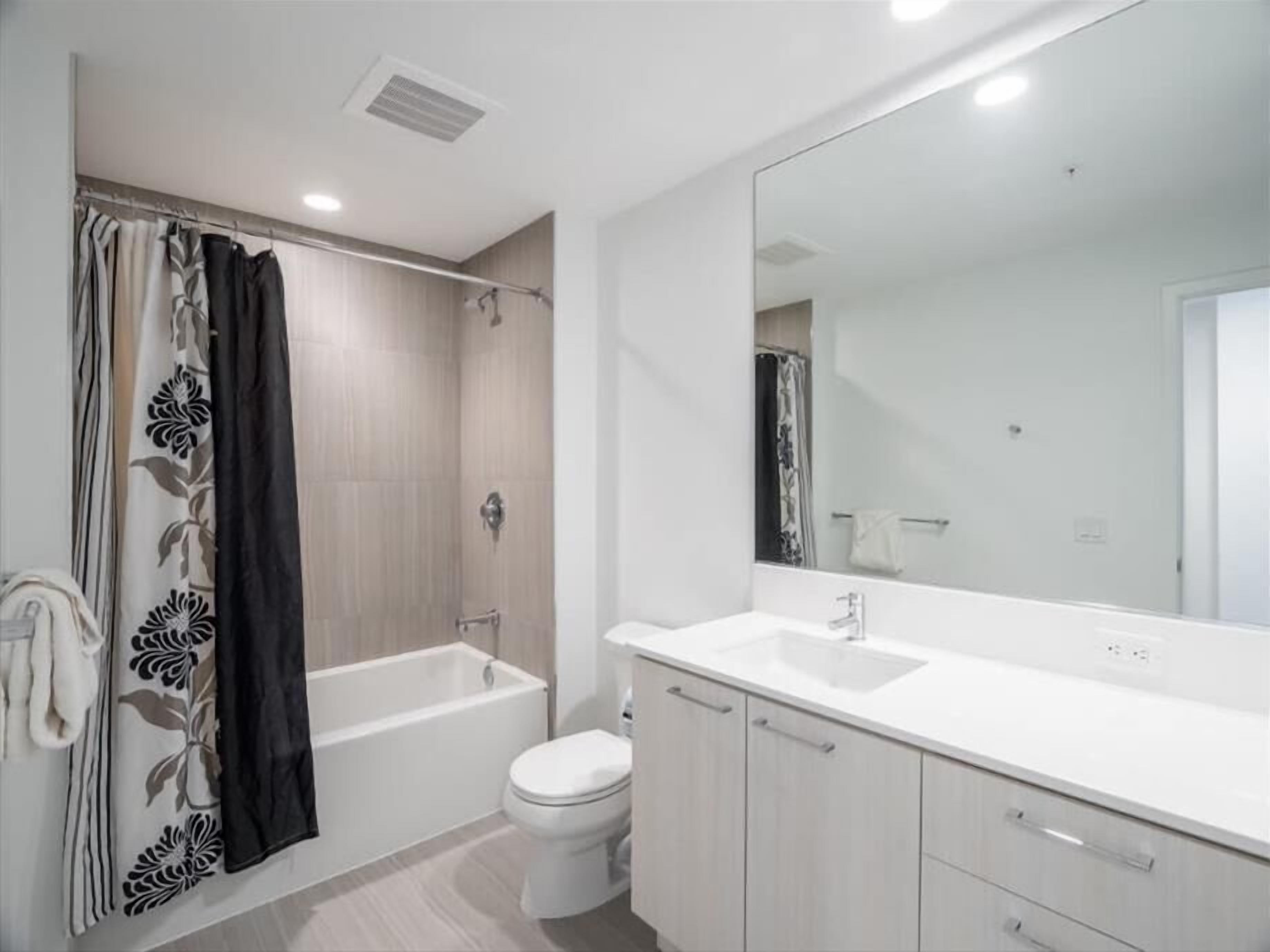 A modern bathroom with a bathtub, toilet, and a large mirror.