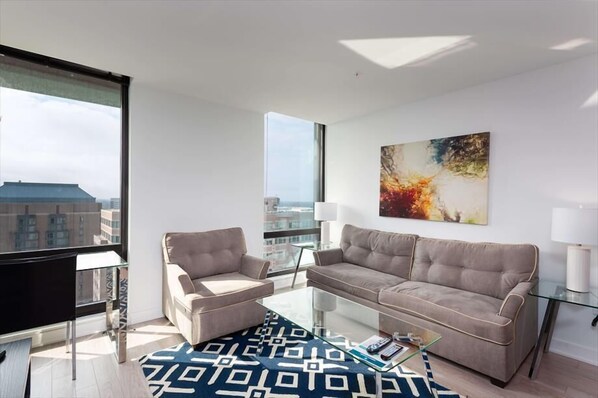 Una sala de estar moderna con un sofá, sillones, una mesa de centro de vidrio y un ventanal con vistas a la ciudad.