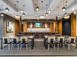 Eine moderne Hotelhalle mit Barbereich in der Mitte, verschiedenen Sitzgelegenheiten und Pendelleuchten.