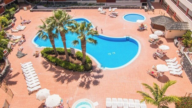 A resort pool area with multiple pools, sun loungers, and palm trees.