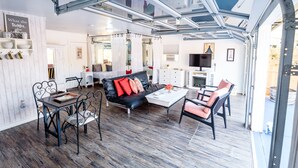 A spacious living area with a black leather sofa, a dining table, and chairs. A large window with metal framing allows natural light to enter. - Romantic retreat walking distance to wineries  (Temecula)