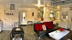 A modern, well-lit room with a black leather sofa, a white table, and a black metal chair. There is a bed with a canopy and a white dresser in the background. - Romantic retreat walking distance to wineries  (Temecula)