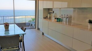 Una cocina moderna con vista al océano, un comedor con mesa de vidrio y un balcón con barandilla.