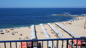 Una playa con sombrillas y tumbonas, una red de voleibol y vista al océano.