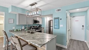 A modern kitchen with a marble island, stainless steel appliances, and a bar area with stools. - Sugar Beach Condos by ALBVR (Orange Beach)