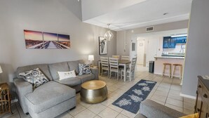 A modern living room with a grey sofa, a round gold coffee table, and a blue rug with sea turtles. - Sugar Beach Condos by ALBVR (Orange Beach)