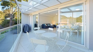 A modern outdoor patio with a glass door leading to a living area, white furniture, and a covered grill.