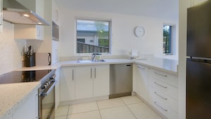A compact kitchen with white cabinets, stainless steel appliances, and a window providing natural light.