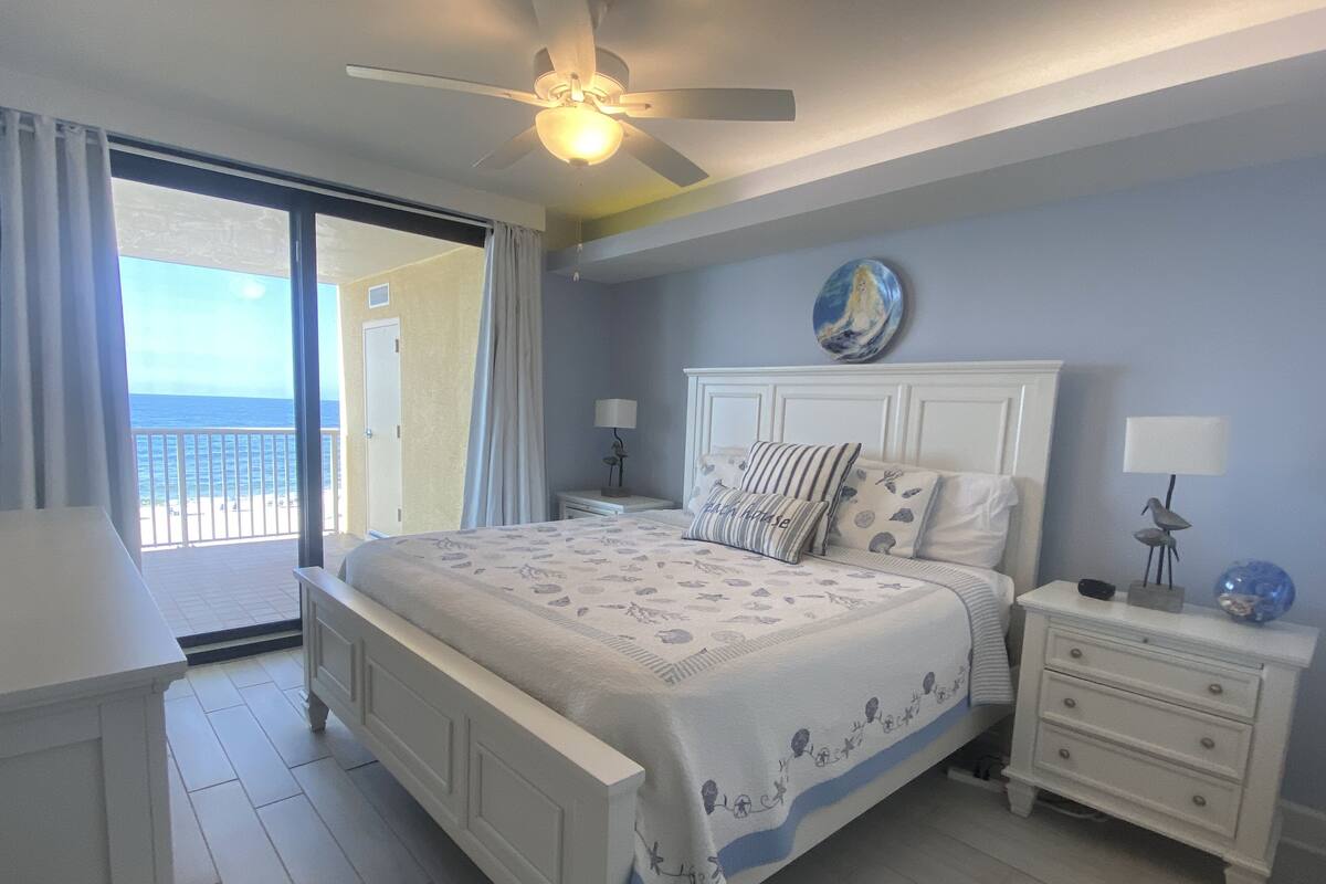 Ein Schlafzimmer mit einem Bett, Nachttischen, einem Deckenventilator und Blick auf den Ozean.