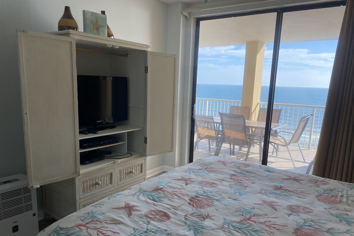 Ein Hotelzimmer mit Bett, Fernseher, Kleiderschrank und einem Balkon mit Meerblick.