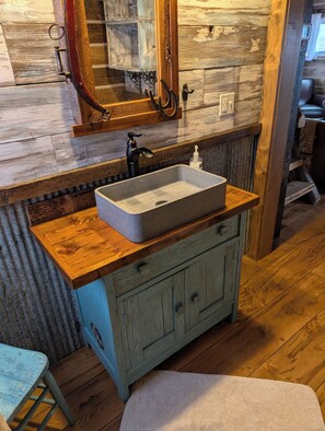 A rustic bathroom with a wooden vanity, a rectangular sink, and a mirror above it.