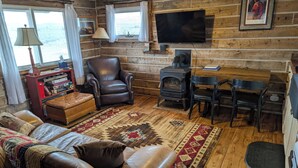 L’intérieur chaleureux d’un chalet avec un canapé en cuir, une table à manger en bois, une cheminée et un téléviseur fixé au mur.
