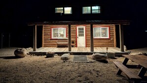 Une cabane en rondins avec deux fenêtres, une porte d’entrée et une véranda.