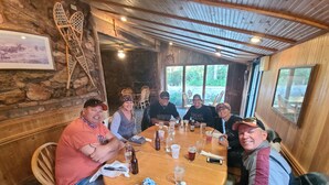 Un groupe de personnes est assis autour d’une table en bois dans un coin repas rustique, avec des murs en pierre et des poutres apparentes.