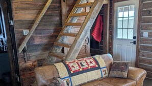 L’intérieur d’un chalet rustique, avec un escalier en bois, un canapé en cuir recouvert d’une courtepointe et un plancher en bois.
