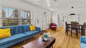 A living room with a blue sofa, wooden coffee table, and a dining area with a red chair and wooden table. - Beaver Street Bungalow w/AC, Fenced Yard, W/D, 4 Smart TVs, 1G WiFi, RV Parking. (Flagstaff)