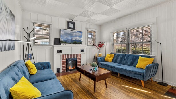A living room with a fireplace, two blue sofas with yellow cushions, a coffee table, and a TV mounted on the wall. - Beaver Street Bungalow w/AC, Fenced Yard, W/D, 4 Smart TVs, 1G WiFi, RV Parking. (Flagstaff)