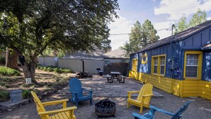 A backyard with Adirondack chairs, a fire pit, a picnic table, and a building with yellow trim. - Beaver Street Bungalow w/AC, Fenced Yard, W/D, 4 Smart TVs, 1G WiFi, RV Parking. (Flagstaff)
