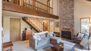 A spacious living area with a high ceiling, a stone fireplace, and a wooden staircase. - Mt Hood Escape, 3 bedroom, 2 bath, plus loft, sleeps 10, hot tub  (Mt Hood Village)
