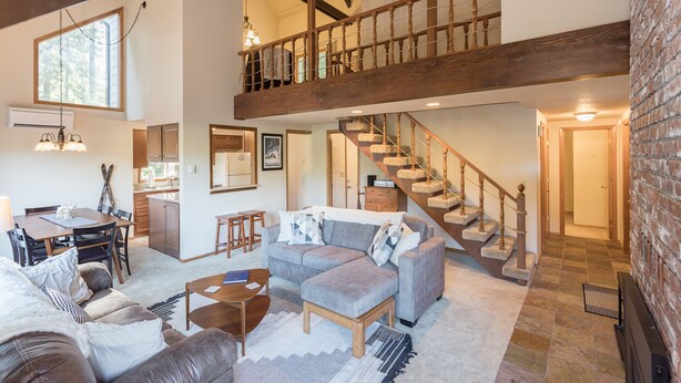 A spacious living area with a high ceiling, wooden staircase, and a dining area with a table and chairs. - Mt Hood Escape, 3 bedroom, 2 bath, plus loft, sleeps 10, hot tub  (Mt Hood Village)