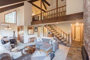 A spacious living area with a high ceiling, wooden staircase, and a dining area with a table and chairs. - Mt Hood Escape, 3 bedroom, 2 bath, plus loft, sleeps 10, hot tub  (Mt Hood Village)