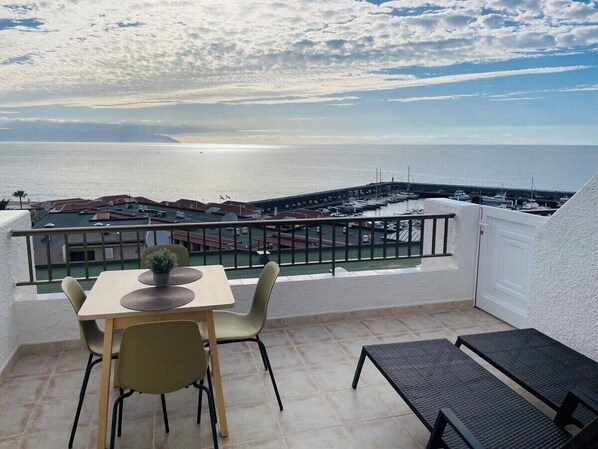 A balcony with a table and chairs, overlooking a marina and the sea. - Ocean view apartment (Santiago del Teide)