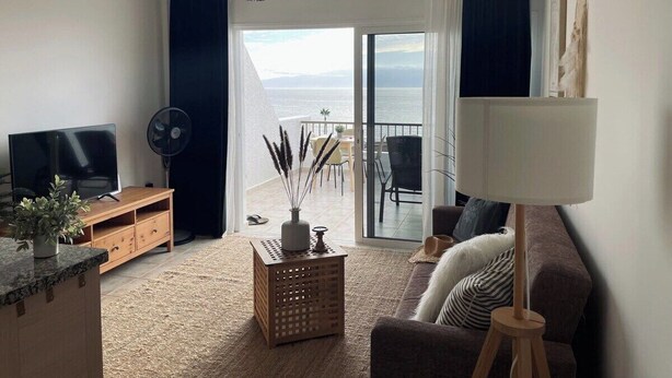 A living room with a TV, sofa, lamp, and a view of the sea through a sliding door. - Ocean view apartment (Santiago del Teide)