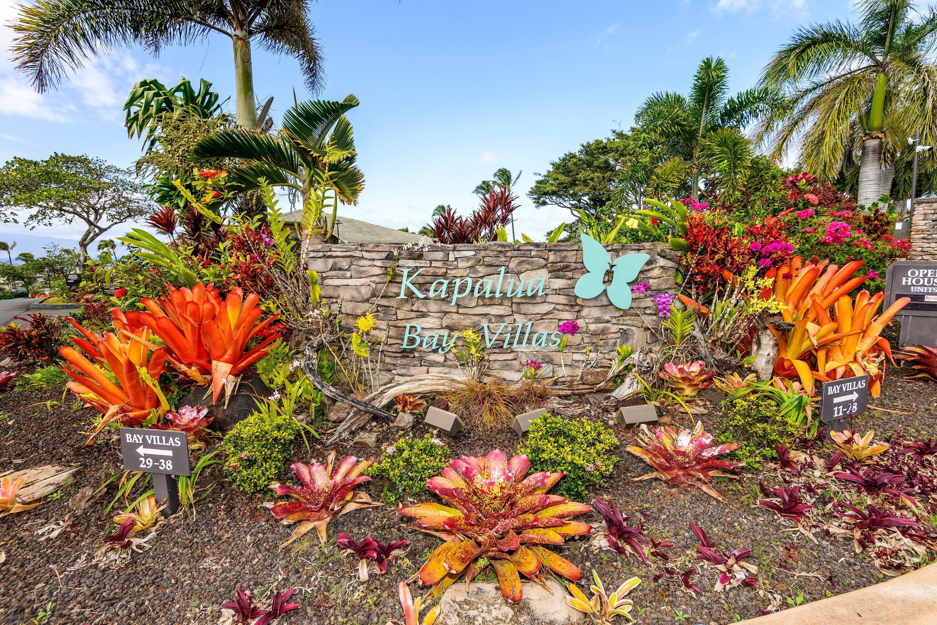 Un mur de pierre sur lequel on peut lire l’inscription « Kapalua Bay Villas », entouré de plantes et de fleurs tropicales.