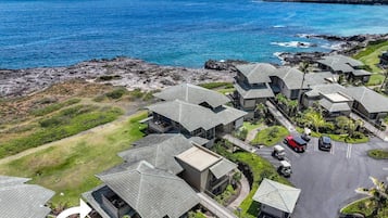 An aerial view of Kapalua Bay Villas 35G1, featuring a cluster of modern villas with sloped roofs, a parking area, and a view of the ocean.