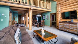 Interior de una cabaña de madera con balcón, comedor y sala de estar con sofá y mesa de centro.