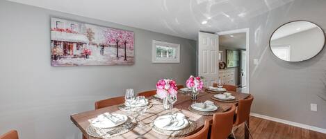 Un coin repas avec une table en bois dressée pour quatre personnes, entourée de chaises orange.