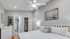 Een slaapkamer met een bed, een plafondventilator, een schilderij en een kledingkast.