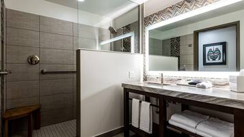 A modern bathroom with a shower, a large mirror, and a vanity with towels.