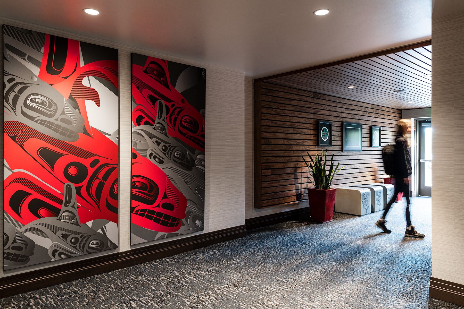 A hallway with a modern design, featuring a large wall mural, wooden paneling, and a potted plant.