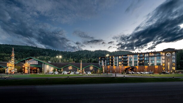 A hotel with multiple buildings, a parking lot, and a forested hill in the background. - 7 Cedars Hotel & Casino (Sequim)