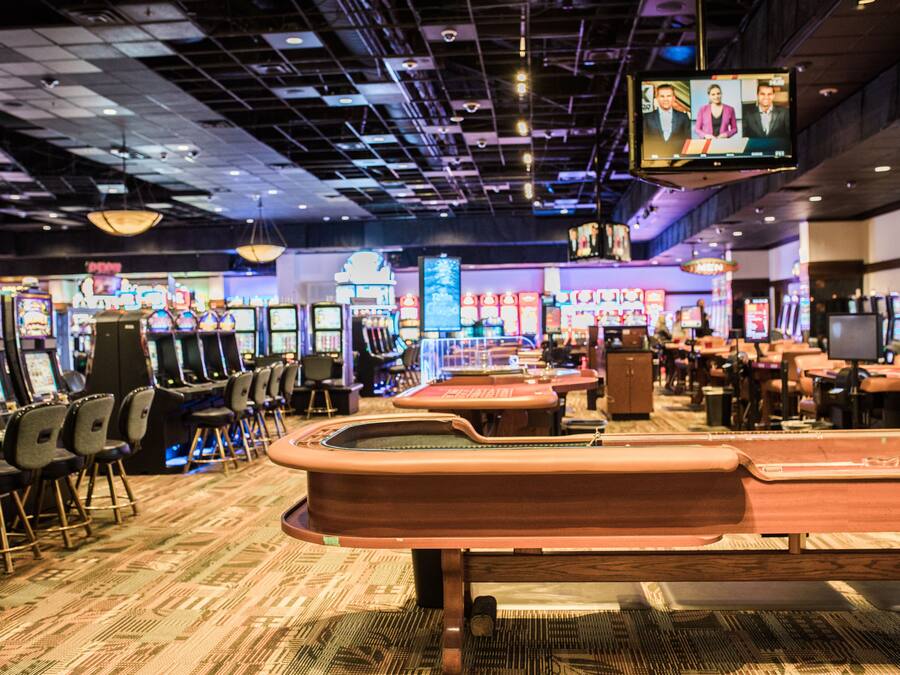 A casino interior with slot machines, gaming tables, and a television displaying a news program.
