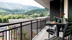A balcony with a table and chairs, a rose vase, and a view of a forested valley with mountains in the background. - 7 Cedars Hotel & Casino (Sequim)