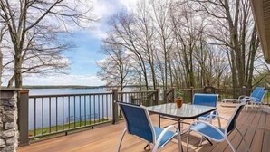 A deck with a table and chairs, overlooking a lake with trees in the background.