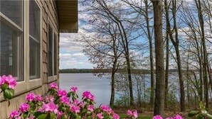 A lakeside view with a wooden cabin and pink flowers in the foreground.