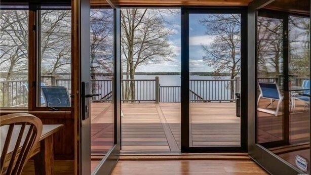 A wooden interior with a sliding glass door leading to an outdoor deck with a view of trees and a body of water.