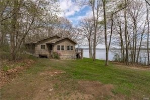 Un chalet rustique doté d’une véranda, entouré d’arbres et bordé par un lac.