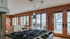 A kitchen with a gas stove, wooden walls, and large windows overlooking a body of water.