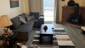 Ein Wohnzimmer mit einer Couch, einem Couchtisch, einer Lampe, einem Kamin und Blick durch eine Schiebetür.