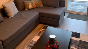 Ein modernes Wohnzimmer mit einem Ecksofa, einem Couchtisch mit Kerze und einem großen Fenster mit Blick auf eine verschneite Landschaft.