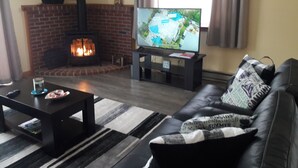 Ein Wohnzimmer mit Kamin aus Ziegelsteinen, einem Fernseher auf einem Standfuß, einem Ledersofa und einem Couchtisch.