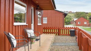 Ein rotes Holzgebäude mit einem Balkon, zwei Metallstühlen und einer kleinen Mülltonne.