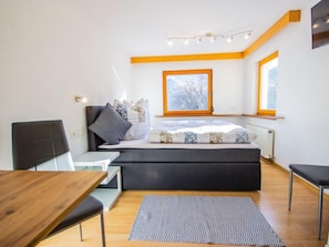 A modern bedroom with a bed, bedside table, chair, and a view of the outdoors through a window.