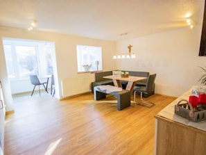 A modern living room with a dining area, wooden flooring, a sofa, a table, and a radiator.