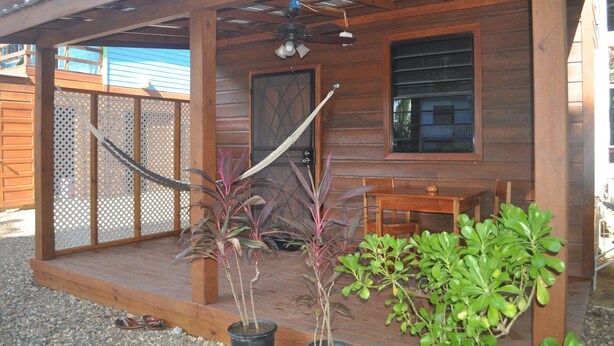 A wooden cabin with a covered porch, a ceiling fan, and potted plants. - Latitude 17 Garden Room, heart of Hopkins Village, Belize (Hopkins Village)